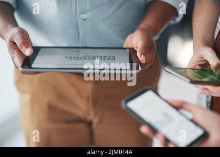 Wer braucht Papier, um an einem erfolgreichen Projekt zu arbeiten. Eine Gruppe von nicht erkennbaren Geschäftsleuten, die während einer Besprechung in einem modernen Büro drahtlose Geräte verwenden. Stockfoto