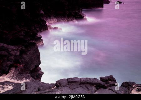 Eine wunderschöne Aussicht auf das geisterhafte Meer an der Kona Coast vor dem roten Abendhimmel auf Kaua'i Island, Hawaii, USA Stockfoto