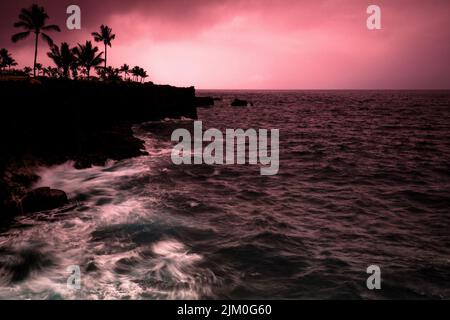 Ein Blick auf Klippen, Felsen und Pflanzen an der Kona Coast vor dem roten Abendhimmel auf Kaua'i Island, Hawaii, USA Stockfoto