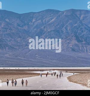 Eine Gruppe von Touristen, die an einem sonnigen Tag in Richtung des Badwater Basin im Death Valley wandern Stockfoto