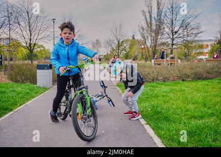 Ein kleiner Junge auf einem Fahrrad und ein anderer auf einem Asphaltweg auf der Suche nach etwas in einem Park im Bezirk Orla Bialego Stockfoto