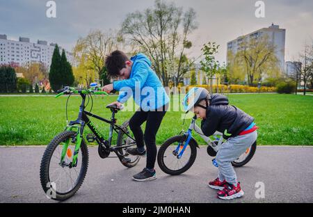 Ein Blick auf zwei kleine Jungen mit ihren Fahrrädern im Garten auf der Suche nach etwas auf einem Asphaltweg Stockfoto