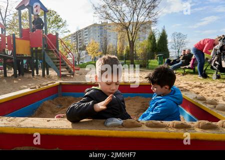 Ein Blick auf zwei kleine Jungen, die mit Plastikspielzeug in einem Sandkasten auf einem Spielplatz spielen Stockfoto