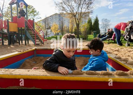 Eine Auswahl von zwei Jungen, die mit Plastikspielzeug in einem Sandkasten auf einem Spielplatz spielen Stockfoto