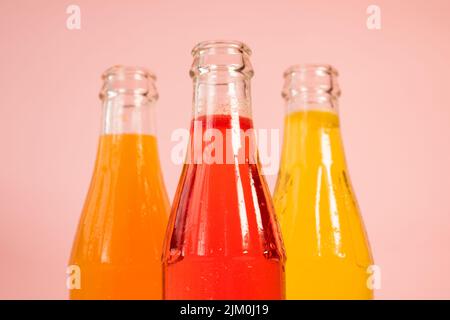 Eine Nahaufnahme von Glasflaschen mit bunten, glitzernden Säften auf einem rosa Hintergrund Stockfoto