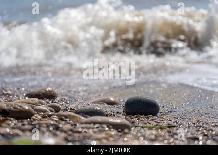 Eine selektive Aufnahme von Kieselsteinen am Strand und einer Welle vor unscharfem Hintergrund Stockfoto