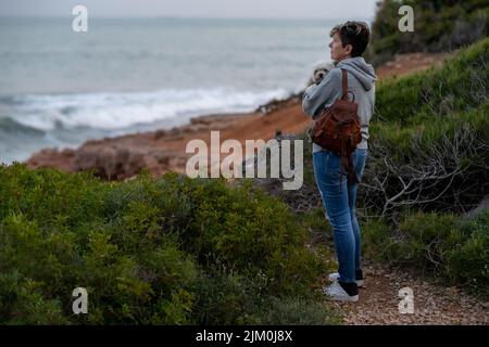 Eine junge Hündin mit ihrem maltesischen bichon, die eine tolle Zeit am Strand von Oropesa del mar in Castellon Spanien hat Stockfoto