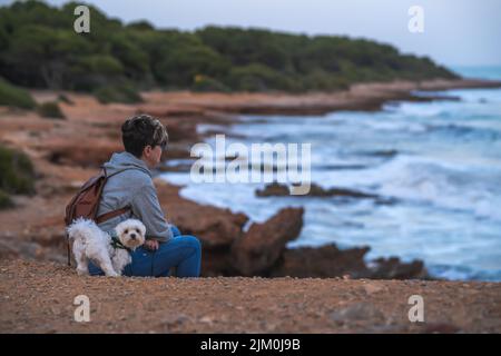 Eine junge Hündin mit ihrem maltesischen bichon, die eine tolle Zeit am Strand von Oropesa del mar in Castellon Spanien hat Stockfoto