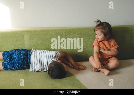 Lachender Bruder spielt mit seiner kleinen Schwester, die zusammen auf dem Sofa im Wohnzimmer zu Hause liegt. Freizeit faul Wochenende Aktivität Spiel mit Kind Freizeit Stockfoto