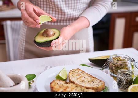 Frau quetscht frischen Limettensaft auf einer halbierten Avocado in der heimischen Küche Stockfoto