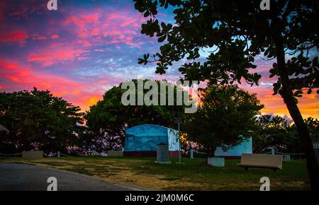 Ein faszinierender farbenprächtiger Sonnenuntergang über einem Park mit grünen Bäumen Stockfoto