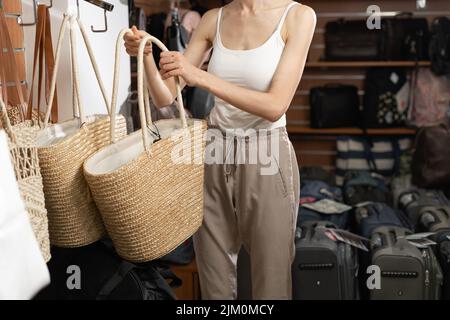 Vitrine im Innenbereich mit gewebten Stricktaschen. Shopper-Frau, die eine Tasche wählt. Stockfoto