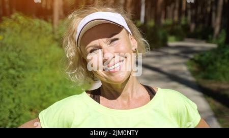 Reife Frau in weißer Mütze sieht die Sonne lächelnd aus der Nähe Stockfoto