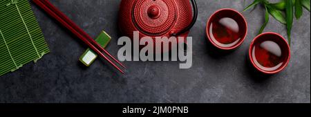 Grüner Tee in Schüsseln und Teekannen und Sushi-Essstäbchen auf dem Steintisch. Draufsicht flach liegend Stockfoto