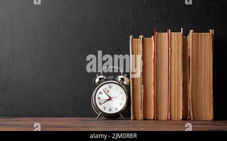 Alte Bücher, Wecker auf Holztisch und Tafel für Kopierplatz. Vorlage für Schule und Bildung Stockfoto