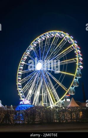 Eine vertikale Aufnahme eines Riesenrades in einem Vergnügungspark bei Nacht mit Neonlicht darauf Stockfoto