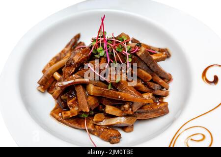 Gebratenes Schweinefleisch in Sauce mit Mikrogemüse verziert. Marinierte Schweineohren. Stockfoto