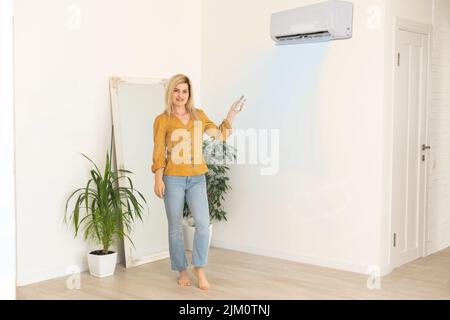 Frau mit Fernbedienung, die auf die Klimaanlage gerichtet ist Stockfoto