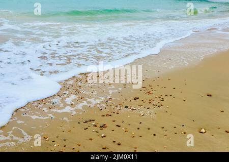 Ein weißer Schaum einer sanften Welle an einem Sandstrand Stockfoto