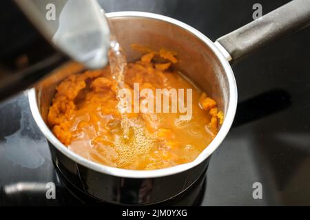 Pürierte Karotten werden mit kochendem Wasser in einen Stahltopf gegossen und kochen eine gesunde, verdauliche Gemüsesuppe, die von Professor Moro gegen Durchfall erfunden wurde, Stockfoto