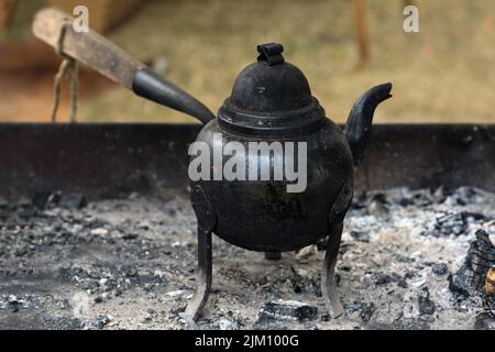 Kleiner Eisenkessel auf drei Beinen mit Holzgriff zum Kochen von Kaffee oder Tee auf offenem Feuer oder Holzkohle, Kopierraum, ausgewählter Fokus, narr Stockfoto