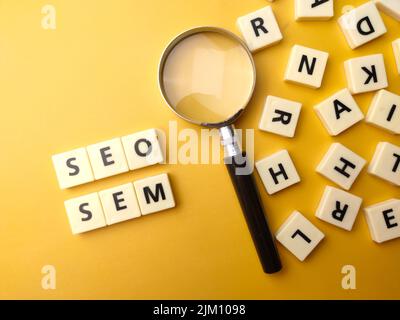 Lupe und Spielzeug Wort mit dem Wort SEO und SEM auf gelbem Hintergrund. Geschäftskonzept. Stockfoto