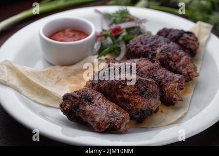 Lammkebab mit Sauce und Kräutern auf einem weißen Teller Stockfoto