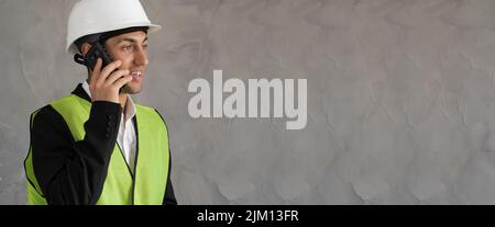 Junge Architektin mit Schutzhelm arbeitet im Baubereich. Vorarbeiter benutzen Smartphone auf Zementwand mit Kopierraum, Banner Stockfoto