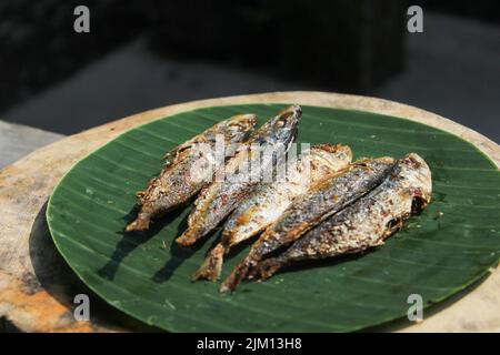 indonesische authentische Lebensmittel gebratener gesalzener Fisch oder ikan asin gereh auf Holzoberfläche mit Bananenblatt. Stockfoto