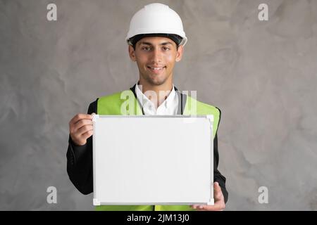 Portrait eines arabischen Ingenieurs mit leerem Raum, männlicher Architekt, der Whiteboard für Text auf grauem Hintergrund hält, Gebäude Stockfoto