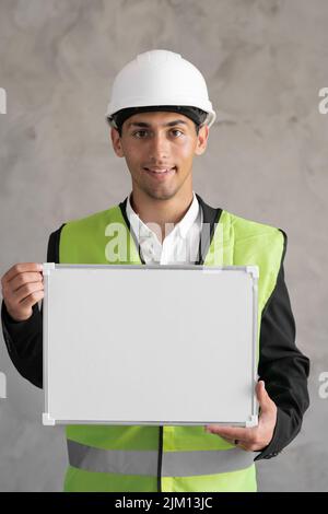 Portrait eines arabischen Ingenieurs mit leerem Raum, männlicher Architekt, der Whiteboard für Text auf grauem Hintergrund hält, Gebäude und Renovierung Stockfoto