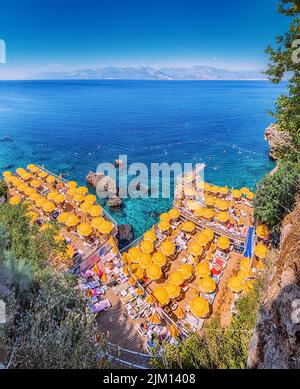 23 June 2022, Antalya, Türkei: Versteckter, enger und gemütlicher Strand zwischen Klippen und Felsen mit leuchtend gelben Sonnenschirmen und Sonnenliegen und landschaftlich erfrischendem Blau Stockfoto