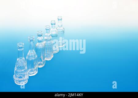 Altmodische Glasflaschen in einer diagonalen Linie auf einem gradienten blau-weißen Hintergrund. Retro abstraktes Thema kreatives Design Konzept. Stockfoto