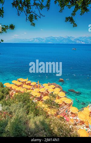 23 June 2022, Antalya, Türkei: Versteckter, enger und gemütlicher Strand zwischen Klippen und Felsen mit leuchtend gelben Sonnenschirmen und Sonnenliegen und landschaftlich erfrischendem Blau Stockfoto
