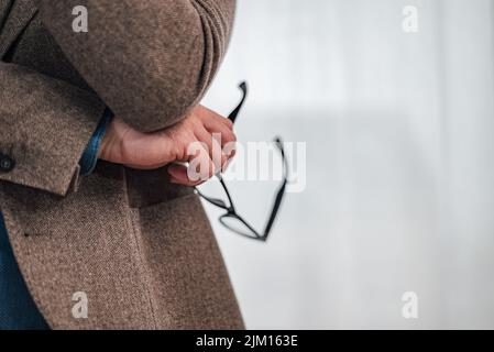 Beschnittenes Bild von professionellen Brillen, die am Arbeitsplatz stehen. Der männliche Unternehmer trägt einen Blazer. Er arbeitet in der Unternehmenszentrale. Stockfoto