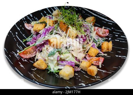 Salat mit Fleisch, Croutons und Gemüse. Schwarzer Teller mit Salat auf weißem Hintergrund. Isolieren. Stockfoto