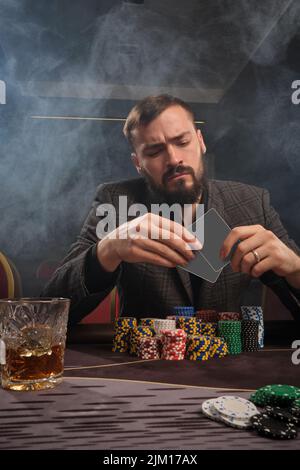 Ein hübscher bärtiger Mann spielt Poker und sitzt am Tisch im Casino. Stockfoto