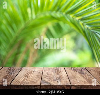 Leere alte Holzdiele Tischplatte und verschwommene grüne Palmenblätter im Hintergrund. Platz für die Produktanzeige. Stockfoto