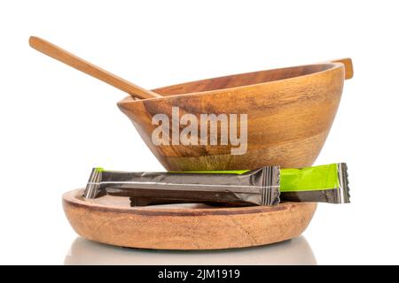 Zwei Zuckerstäbchen in Papiertüten mit einer Holztasse auf einer Holzuntertasse, Nahaufnahme, isoliert auf weißem Hintergrund. Stockfoto