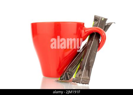 Zwei Zuckerstäbchen in einem Papierbeutel mit einer roten Keramikschale, Nahaufnahme, isoliert auf weißem Hintergrund. Stockfoto