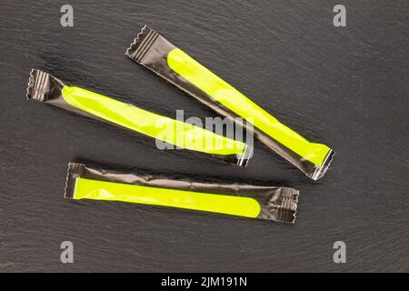 Drei Zuckerstäbchen in Papiertüten auf einem Schieferstein, Nahaufnahme, Draufsicht. Stockfoto