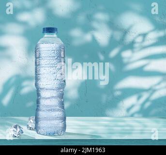 Plastikflasche mit gekühltem Wasser mit Kondensationstropfen und zwei Eiswürfeln auf dem Tisch. Blauer Hintergrund. Stockfoto