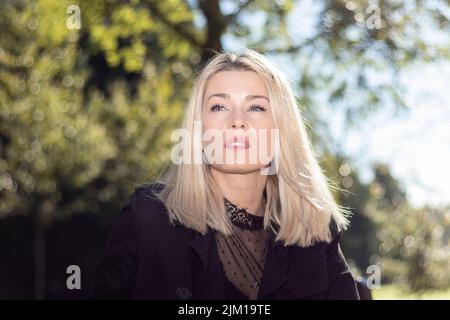 Nachdenkliche blonde Frau, die in einem Park geradeaus schaut Stockfoto