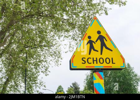 Schulkreuzung Straßenschild. Gelbes Dreieck Warnung für Schulzone Verkehrsschild in den Niederlanden, Bäume im Hintergrund Stockfoto