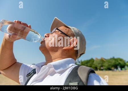 Ein älterer Mann trinkt viel Wasser an einem rekordverdächtigen heißen Sommertag, um Austrocknung unterwegs zu vermeiden. Stockfoto