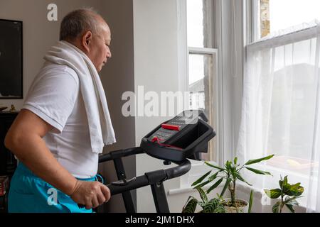 Ein älterer Mann, der zu Hause auf dem Laufband fit bleiben möchte. Stockfoto