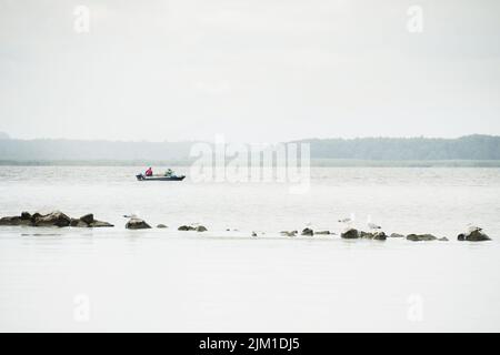 Zwei Fischer auf dem Boot fischen im Paliastomi See mit Möwen stehen auf Felsen im Vordergrund Stockfoto