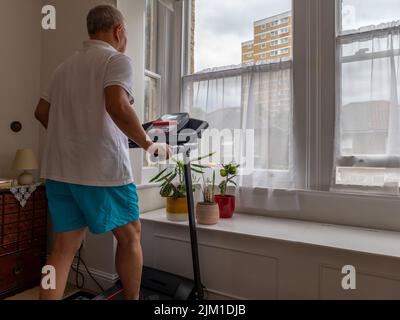 Ein älterer Mann, der zu Hause auf dem Laufband fit bleiben möchte. Stockfoto