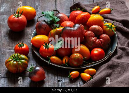 Tomaten verschiedener Sorten und Größen auf einem eisernen Tablett auf einem Holztisch. Stockfoto