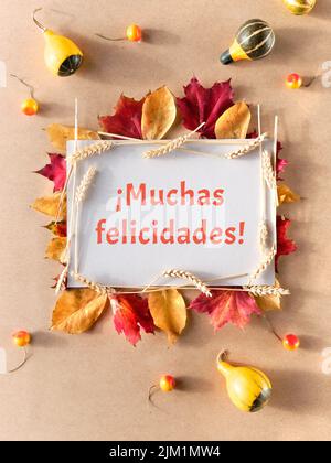 Herbstrahmen, Bildunterschrift Grußtext Muchas felicidades bedeutet Glückwünsche in spanischer Sprache. Flache Lage mit natürlichen Herbstblättern, Stockfoto